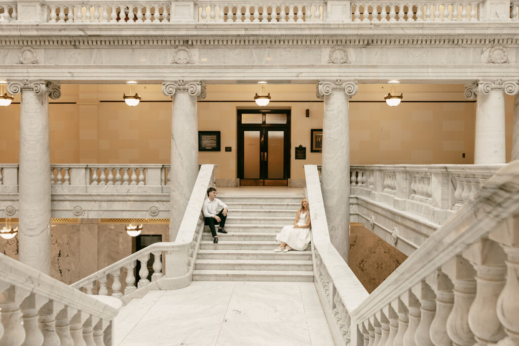 Couple sitting apart on stairs inside Capitol for a candid, stylish moment