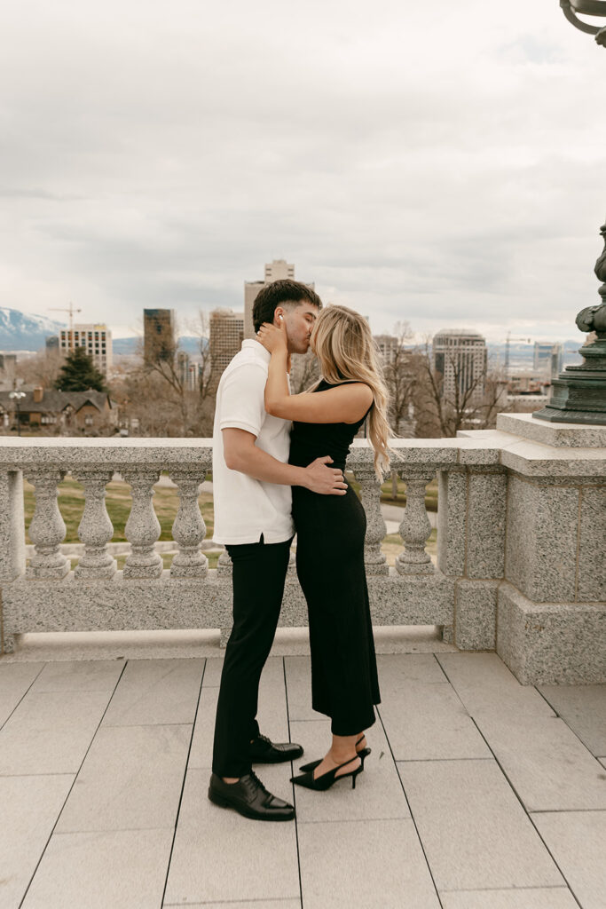 Couple shares a kiss on the Capitol balcony with Salt Lake City skyline in view
