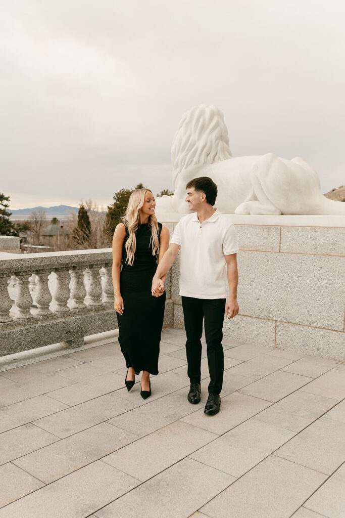 Couple walking hand in hand near marble lion statue on Utah Capitol terrace