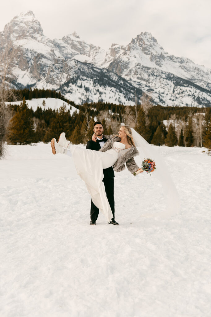 Groom lifts bride playfully in the snow with Grand Teton peaks in the background