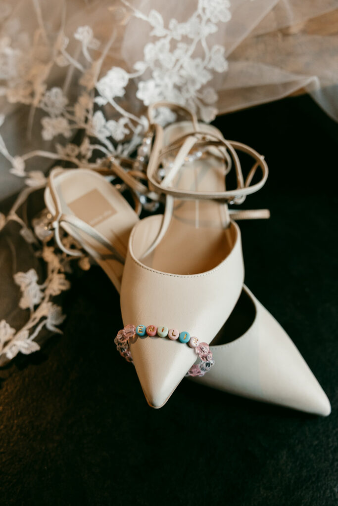 White bridal heels and a beaded bracelet with "Emilie" rest atop delicate lace fabric