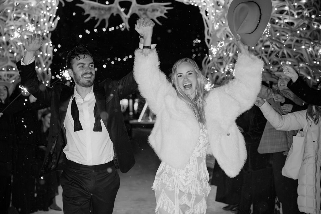 Bride and groom beam with joy during their sparkler send-off under the Jackson Hole antler arch