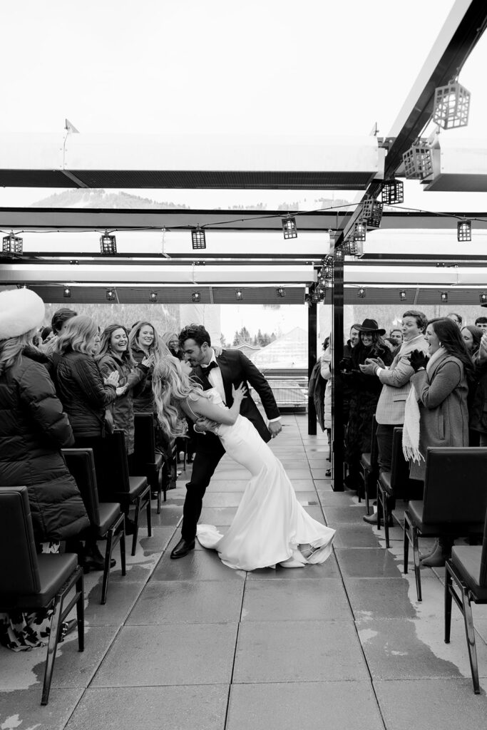 Groom dips bride for a kiss as guests cheer after their Jackson Hole Cloudveil wedding ceremony