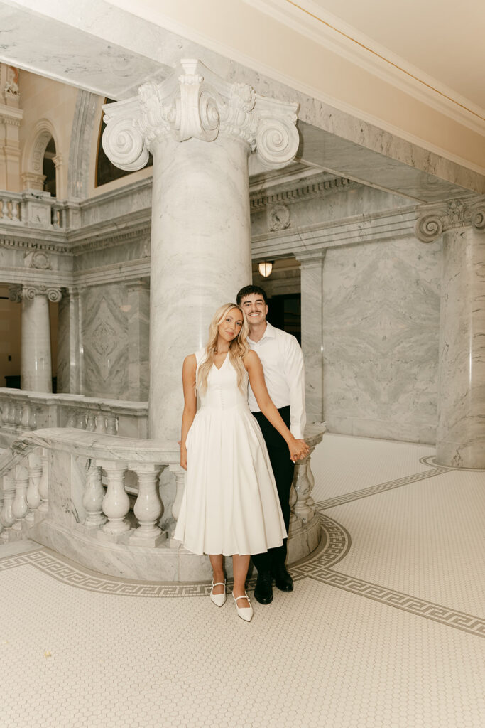 Couple holding hands and smiling beside a marble column inside Capitol