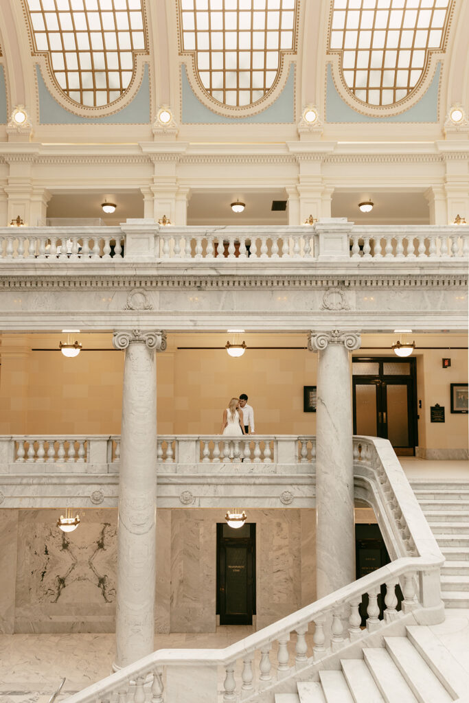 Wide view of couple framed on upper balcony of the Capitol’s grand staircase