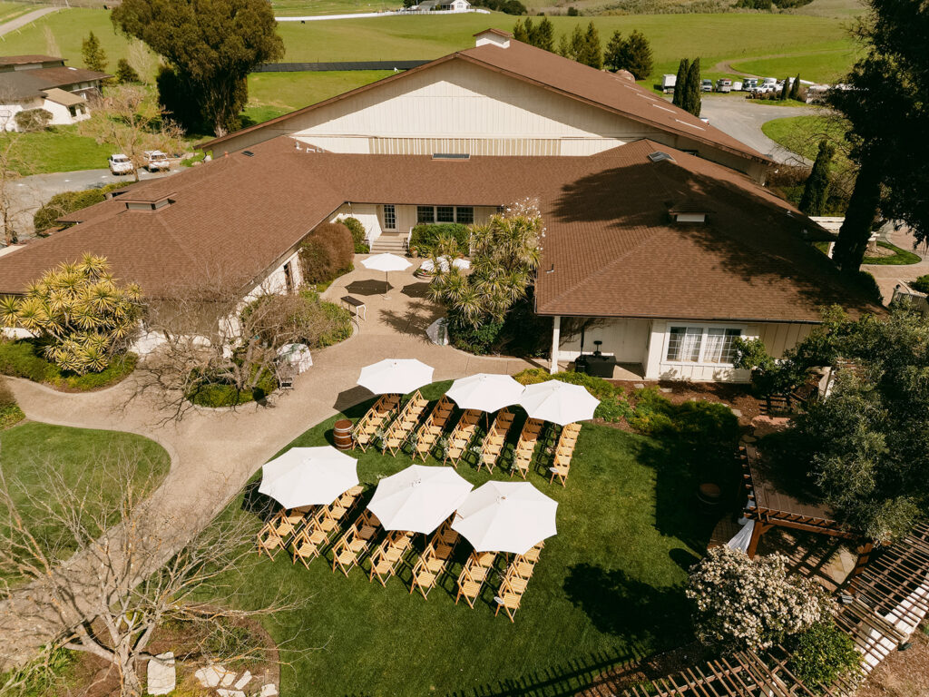 Aerial view of Flying Cloud Farm’s ceremony setup with white umbrellas and folding chairs on green grass