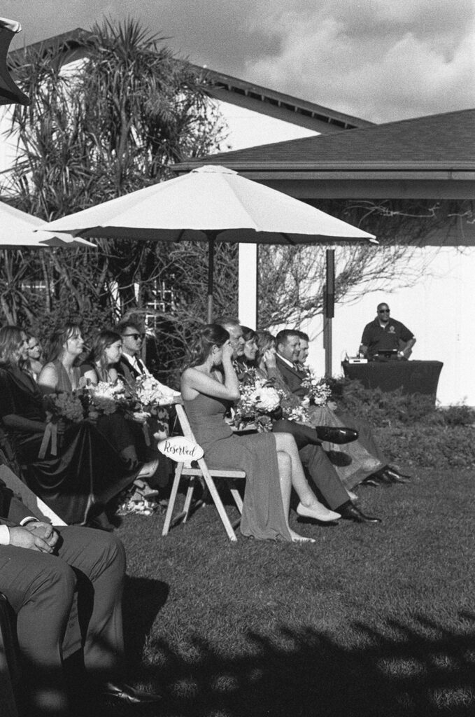 Guests sit beneath umbrellas at the ceremony, capturing a heartfelt moment during the outdoor vows