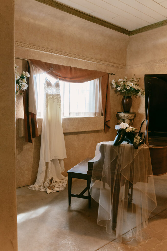 Bride’s lace gown and groom’s shoes styled on a piano bench in the venue’s vintage getting-ready room