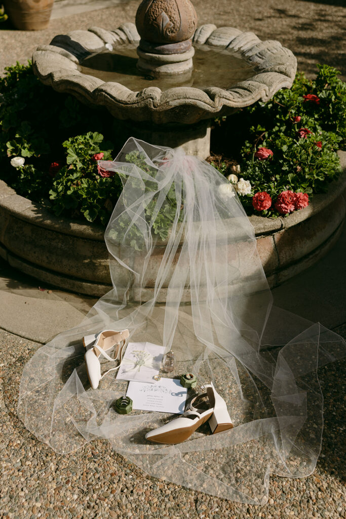 Bridal details, including shoes and perfume, laid out on tulle by a fountain at Sonoma County destination wedding