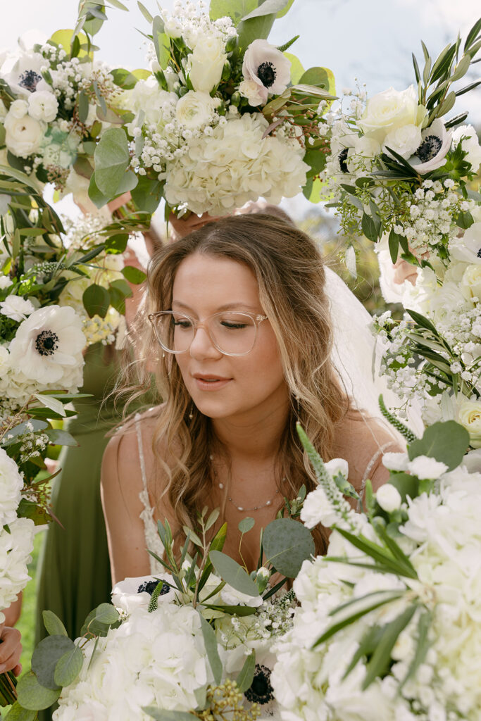 Bride surrounded by white florals, framed in a floral arch as she takes a quiet moment before the ceremony