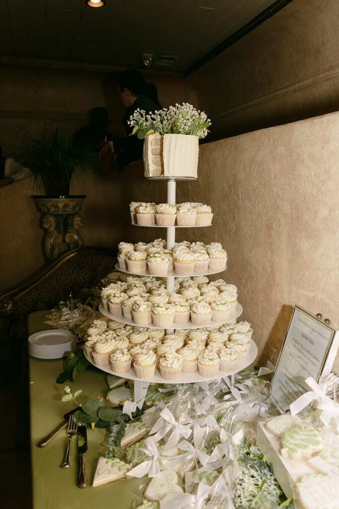 Tower of cupcakes topped with a small cake decorated with white flowers and greenery.
