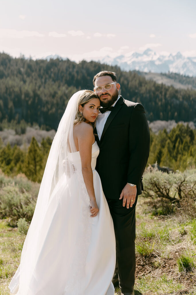 Bride and groom pose with mountain views behind them during golden hour.