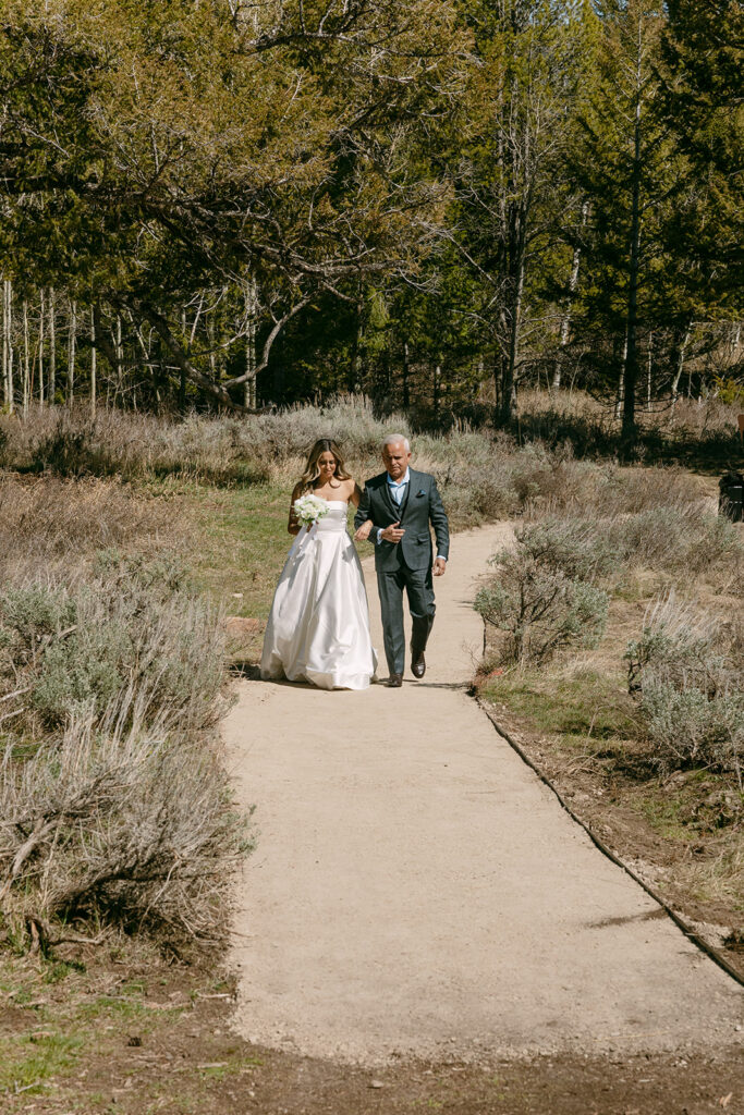 Bride walks through trees toward a Wyoming Wedding Tree elopement ceremony.