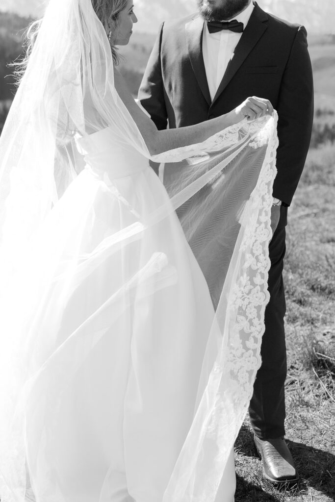 Bride holds veil while facing groom, lace detail softly highlighted.