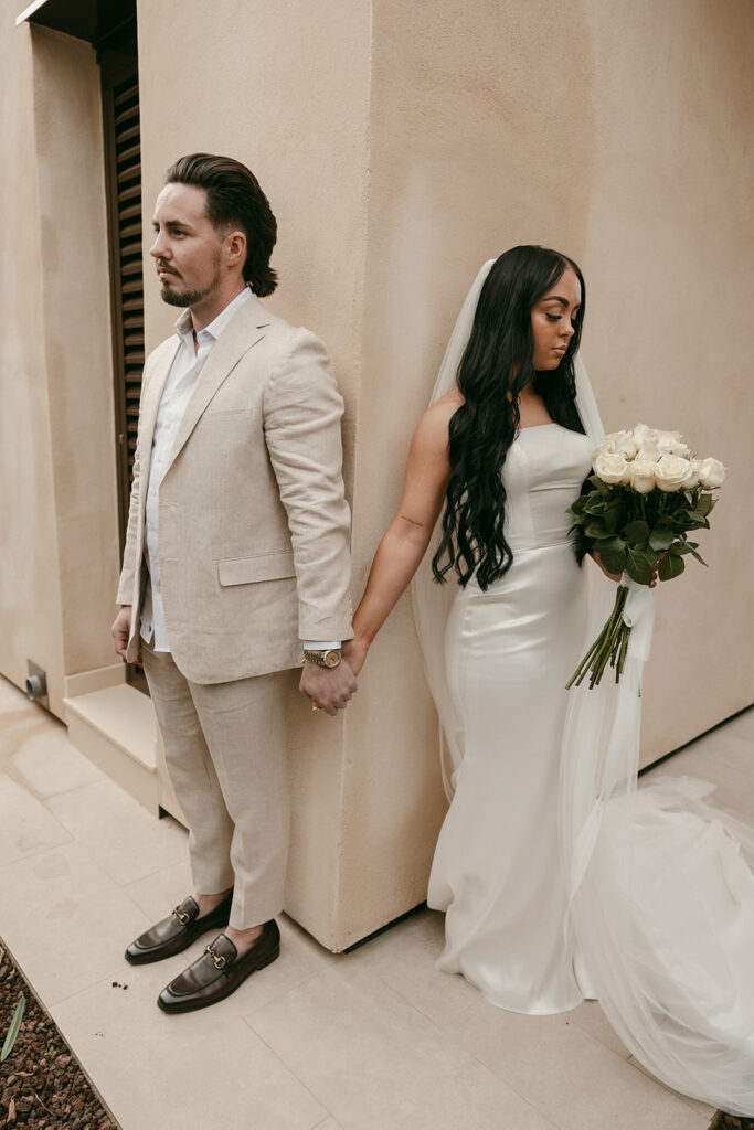First touch moment with bride and groom holding hands around villa corner