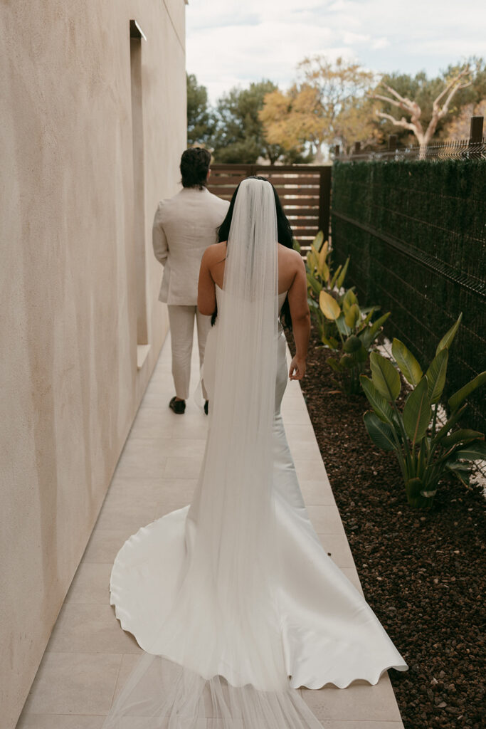 Bride walks toward groom in hallway before their first look, her veil and train flowing behind her