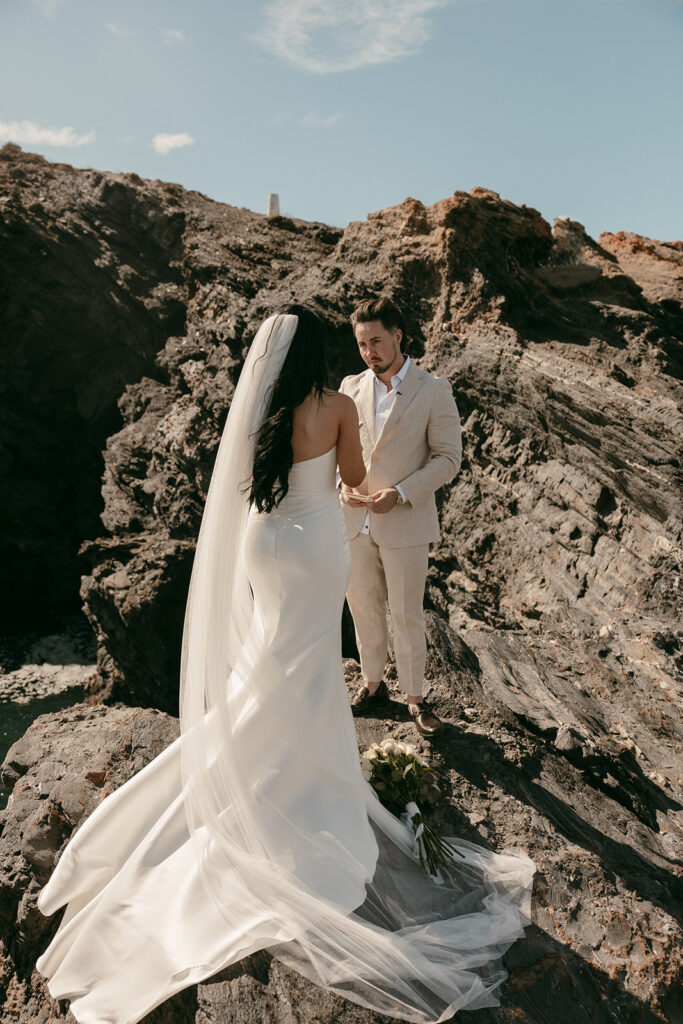 Bride and groom exchange vows on a cliffside with sunlight illuminating the rugged rocks