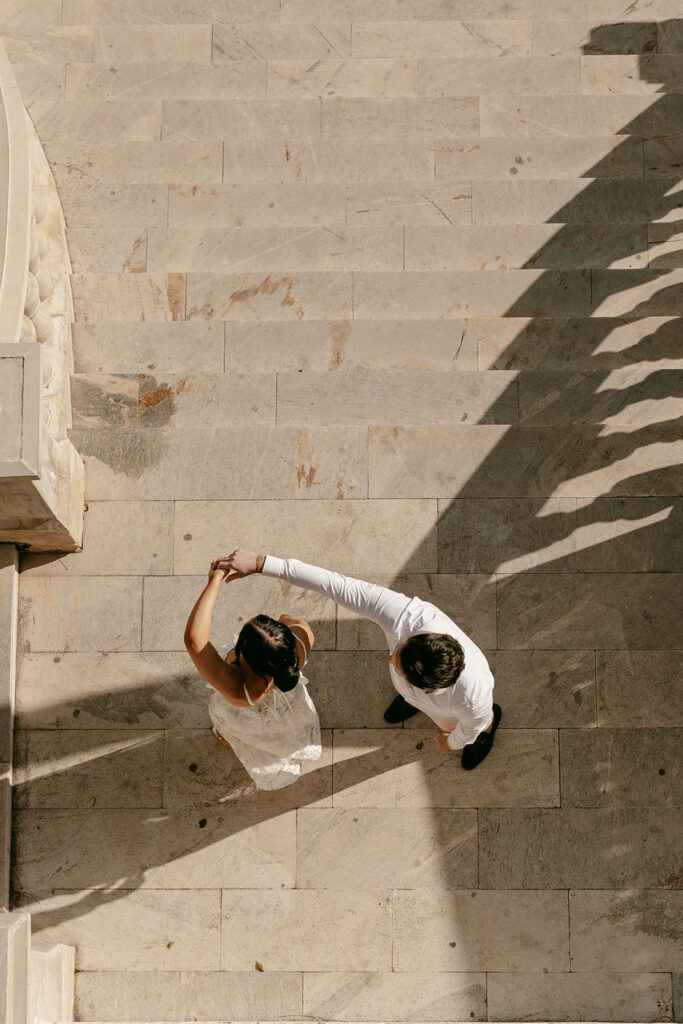 Couple dances on sunlit terrace, captured from above with long shadows stretching across the stairs