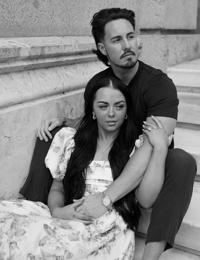 Black and white portrait of couple cuddled on marble steps during pre-elopement session