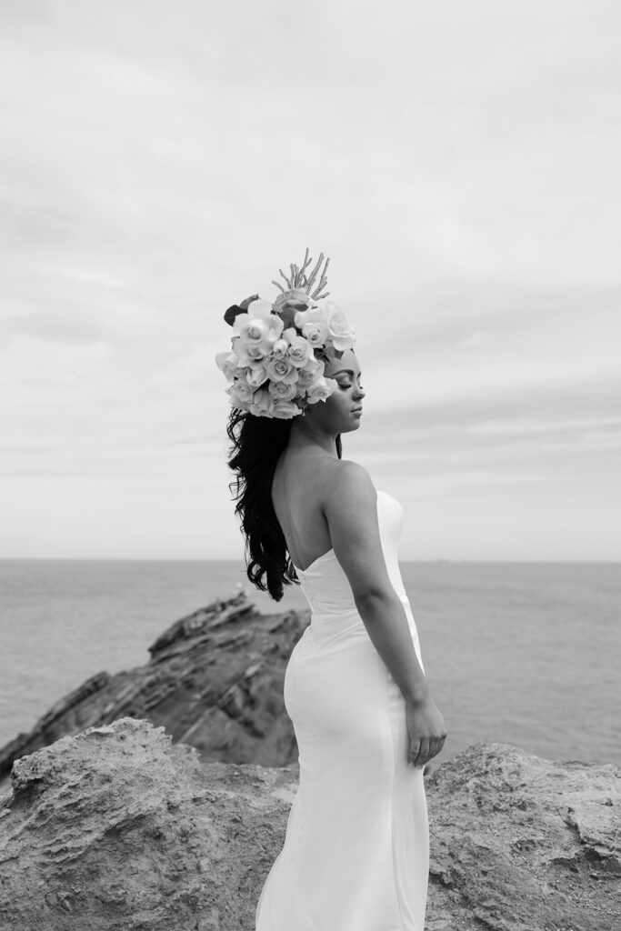 Bride stands on a seaside cliff using bouquet as floral headpiece during Cartagena destination luxury elopement