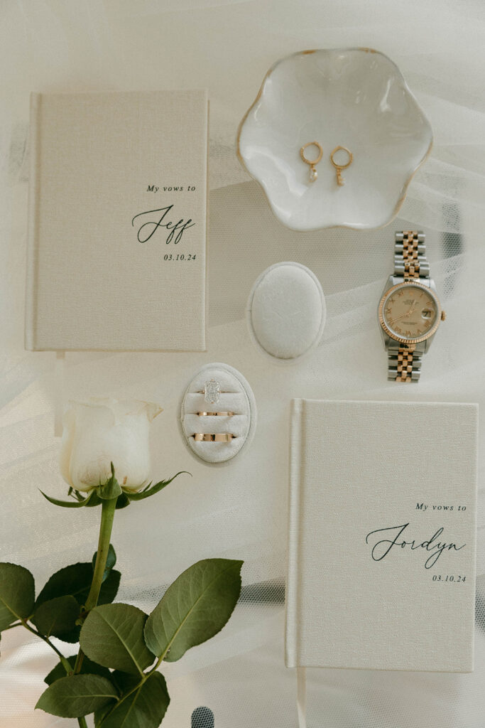 Elegant vow books, jewelry, and white rose flat lay before intimate ceremony