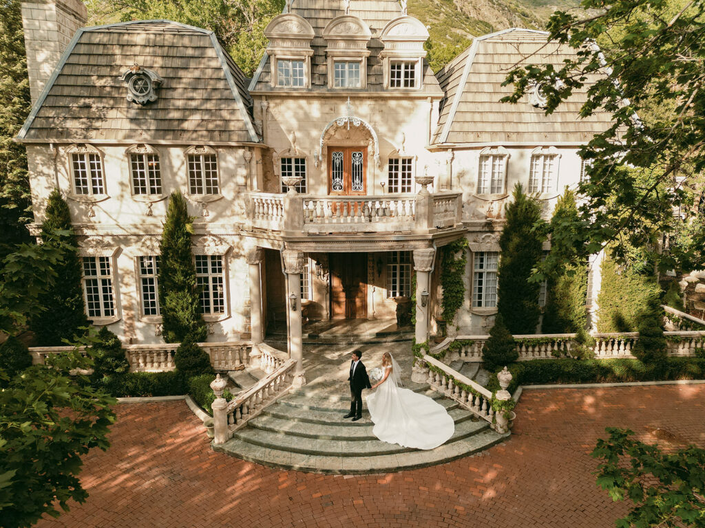 Bride and groom stand on the grand stone steps of La Caille framed by elegant exterior architecture