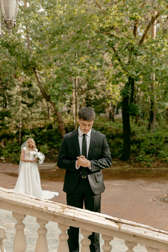 Groom waits with folded hands as bride approaches for first look during La Caille bridal portraits