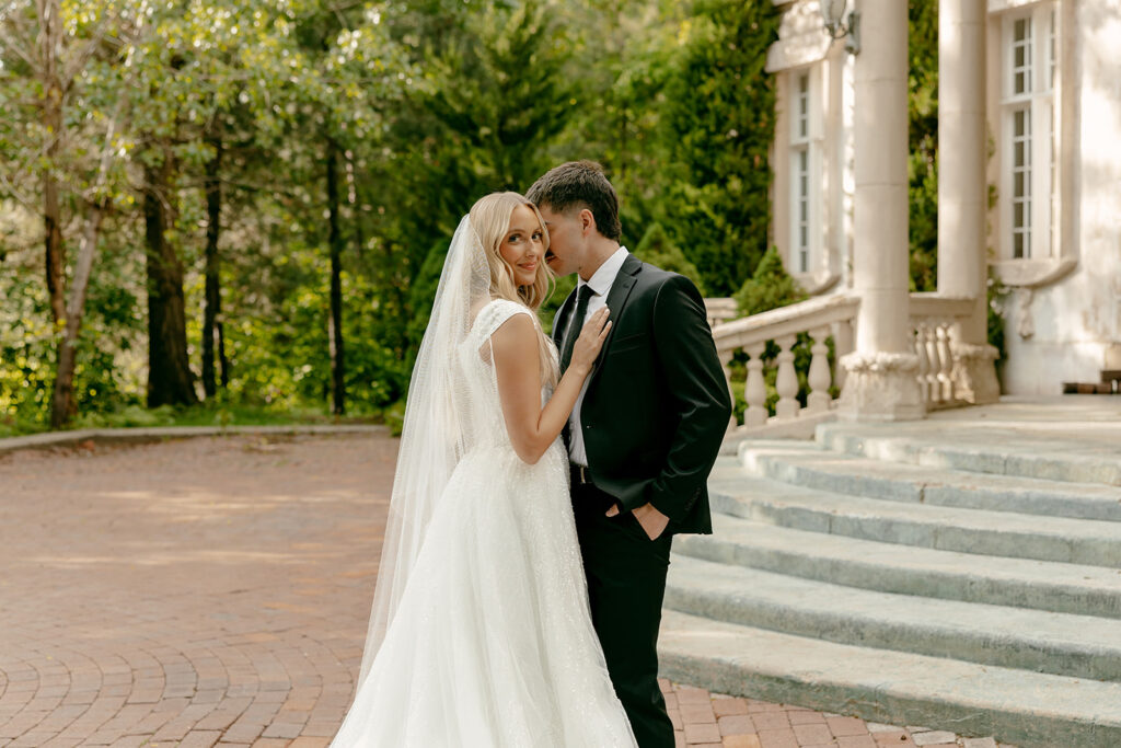 Bride smiles at the camera while the groom leans in lovingly during La Caille bridal portraits