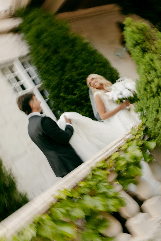 Groom twirls bride mid-laugh on brick path during joyful moment at La Caille