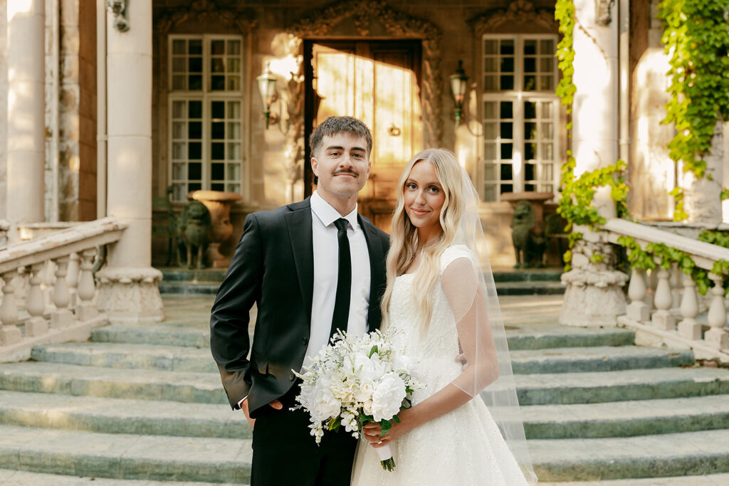 Couple standing side by side in front of ivy-covered stone steps