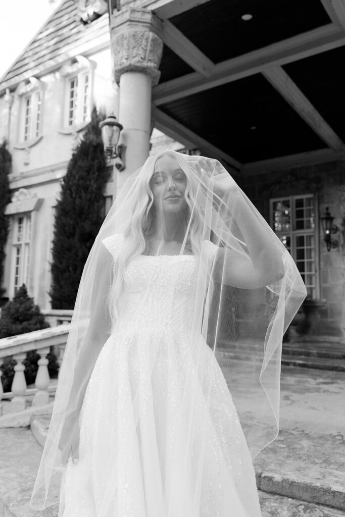 Black and white portrait of bride holding her veil near the villa’s entrance