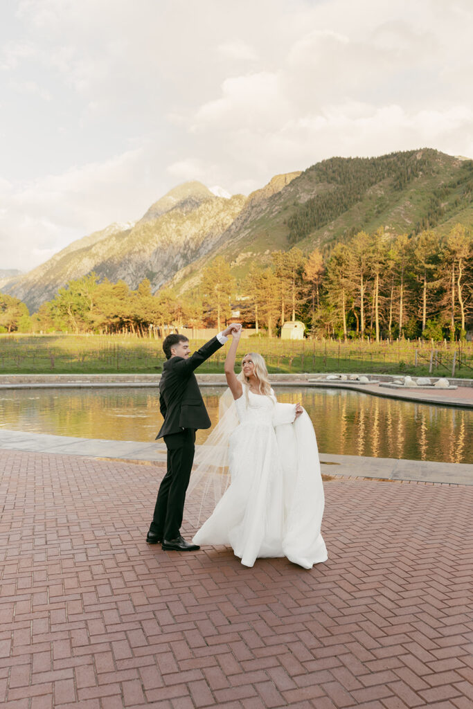 Bride twirls joyfully with her groom beside a vineyard pond