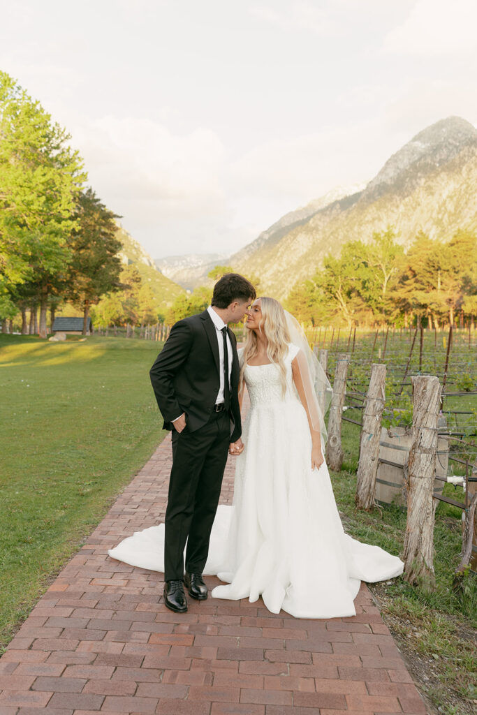 Couple kisses along a vineyard path with mountains in the background for La Caille bridal portraits