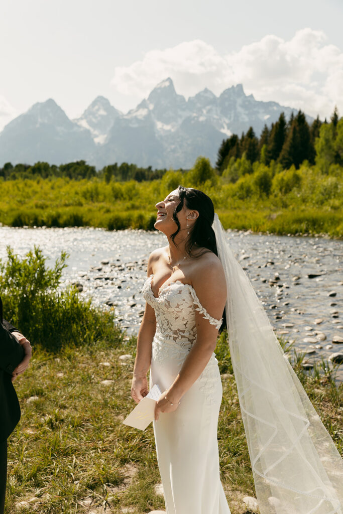 Bride laughs with vow book in hand and Snake River in the background