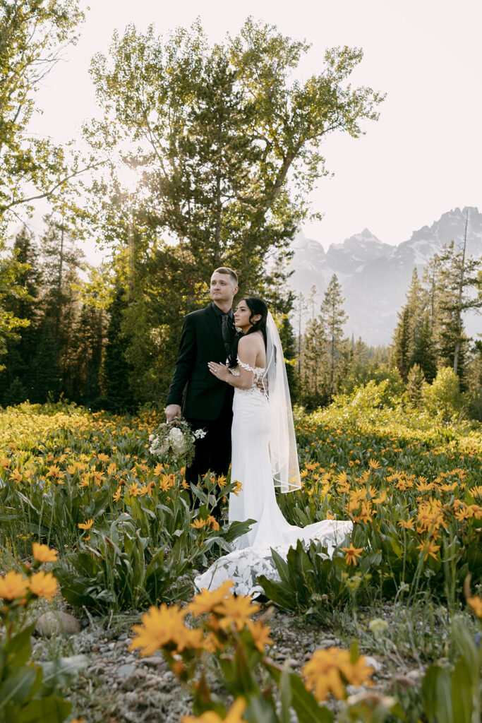 Bride and groom pose amid wildflowers with Grand Teton mountains behind