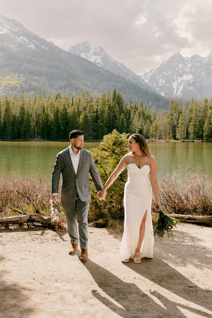 Bride and groom walk hand in hand beside String Lake
