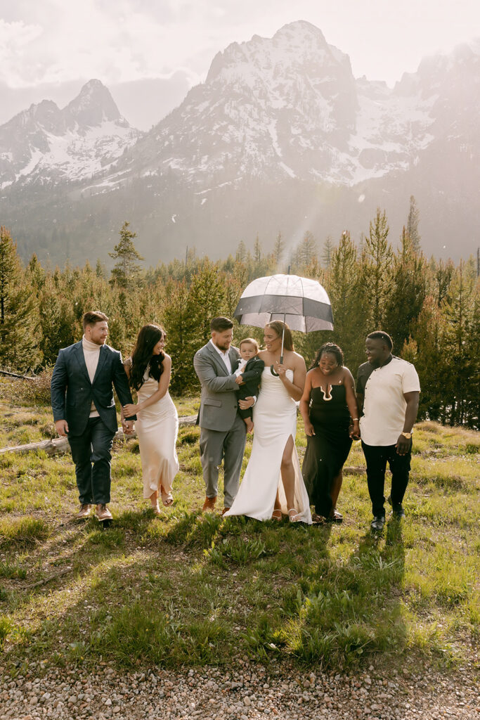 Bride holds umbrella as bridal party walks away from the foot of the Tetons mountain range