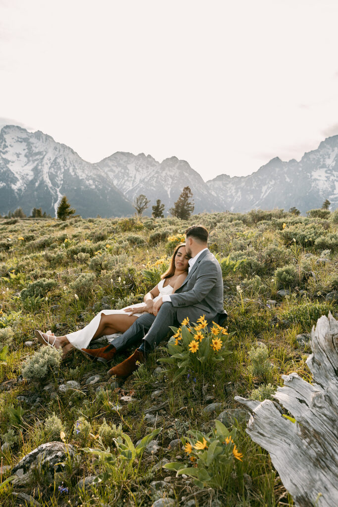 Bride and groom lounge among wildflowers with the Grand Teton range in background