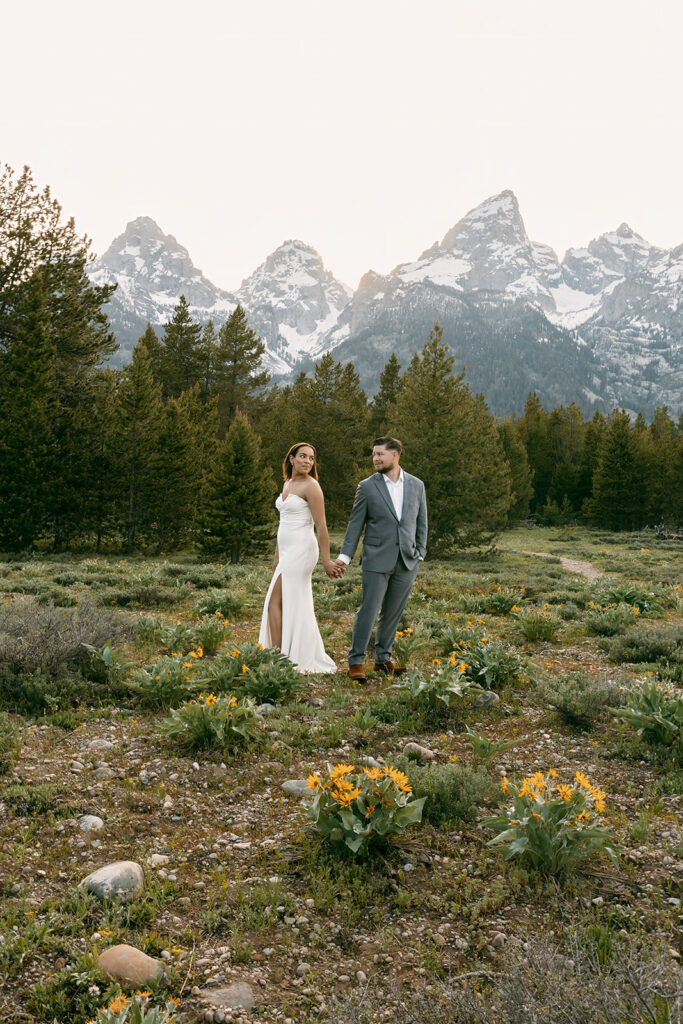 Bride and groom look back over their shoulders at each other while holding hands