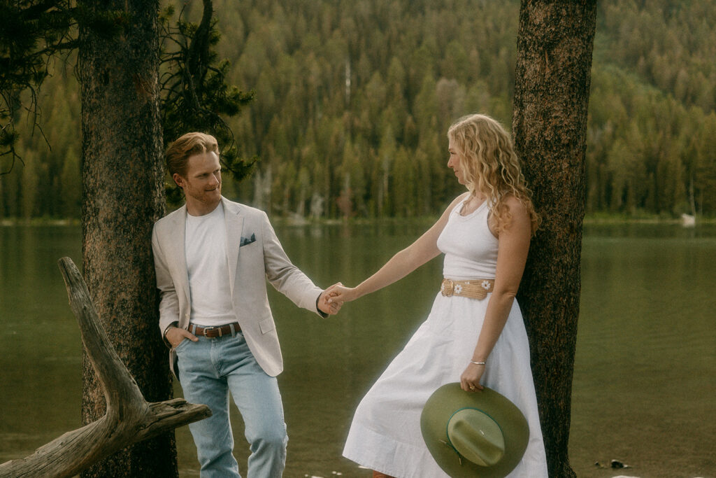 Couple holds hands beside lake during romantic Tetons engagement photography shoot