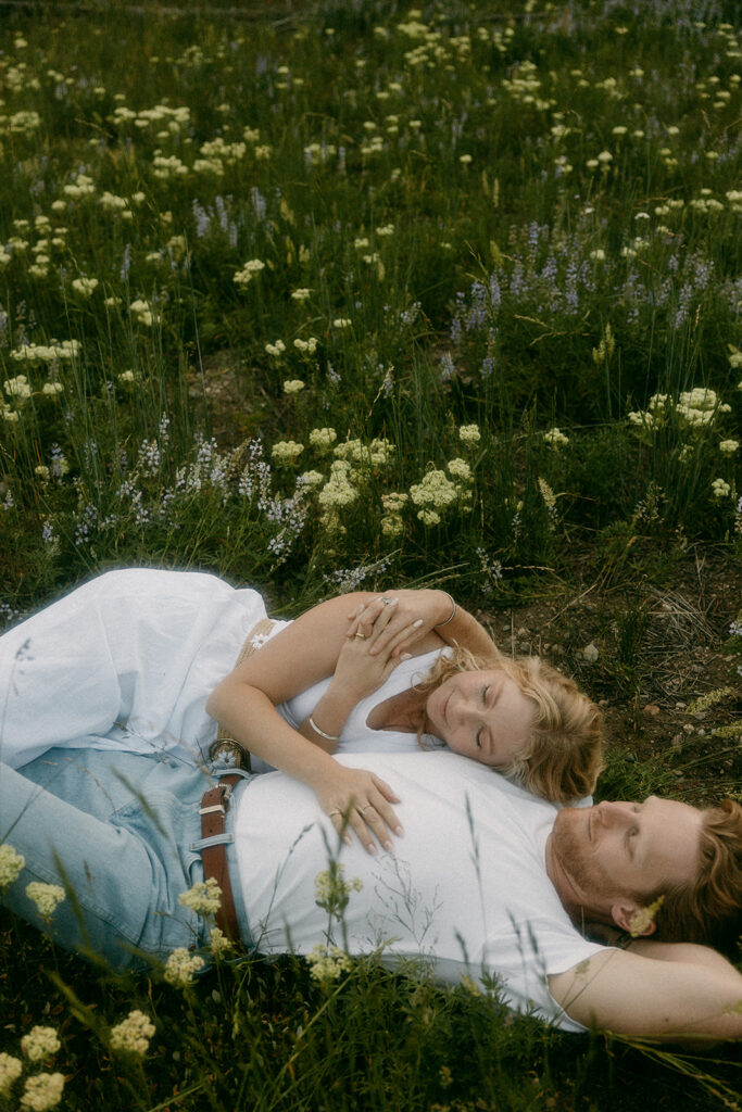 Couple relaxing in a meadow during romantic Tetons engagement photography session