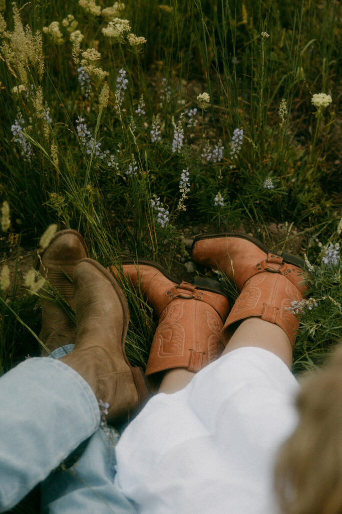 Two pairs of legs with cowboy boots lying in a wildflower meadow