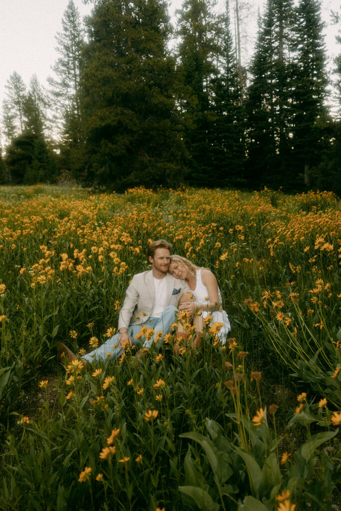 Engaged couple sitting in a vibrant wildflower field during romantic Tetons engagement photography shoot