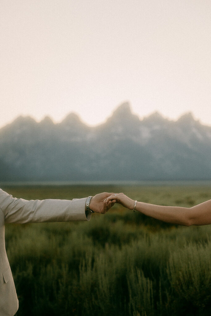 Close up of couple's clasped hands with the Grand Tetons in background