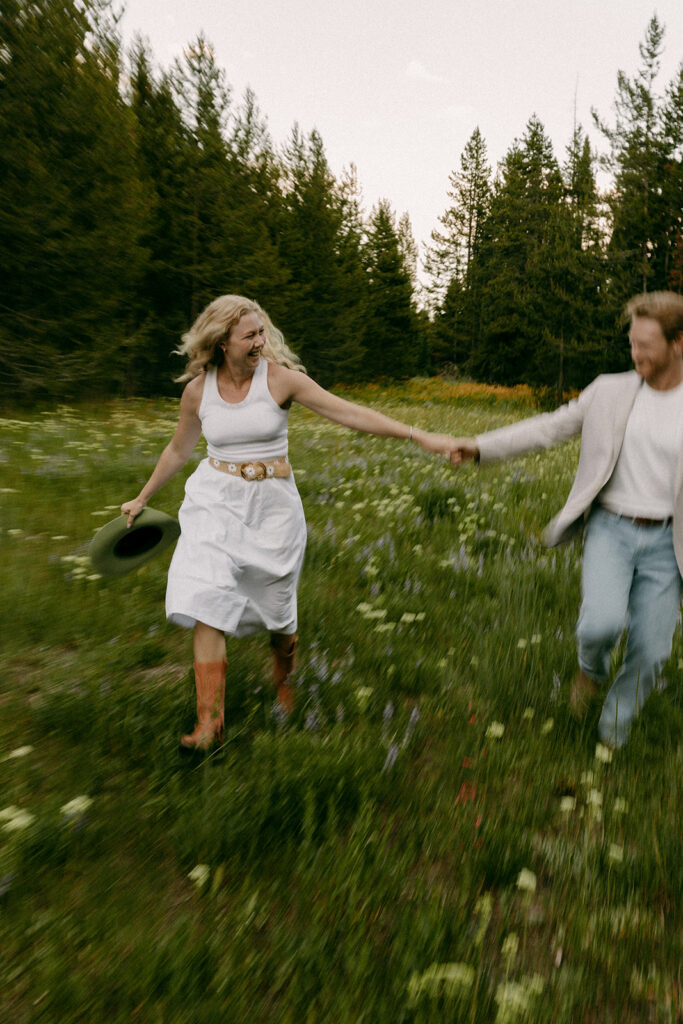 Engaged couple running through an open meadow in Grand Teton National Park