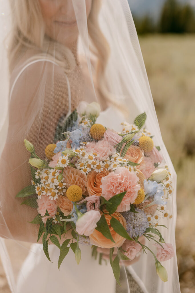Bride holds her wild-flower inspired bouquet under sheer veil