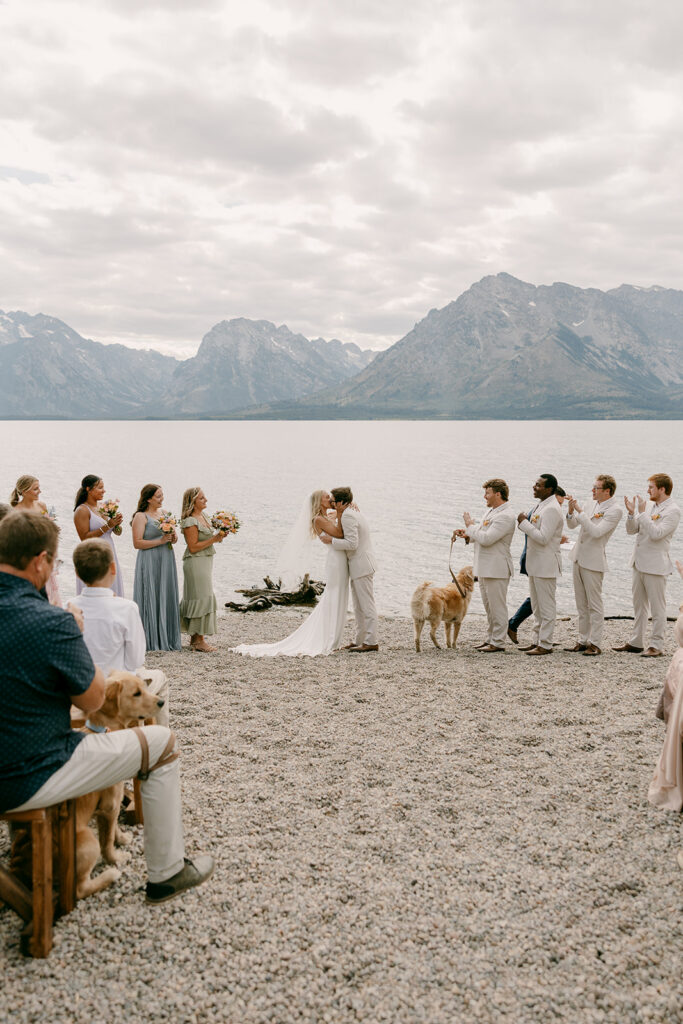 Bride and groom share waterfront first kiss during Jackson Lake Lodge wedding ceremony