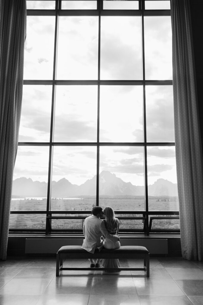 Bride and groom sit inn front of double height window with views of the Tetons