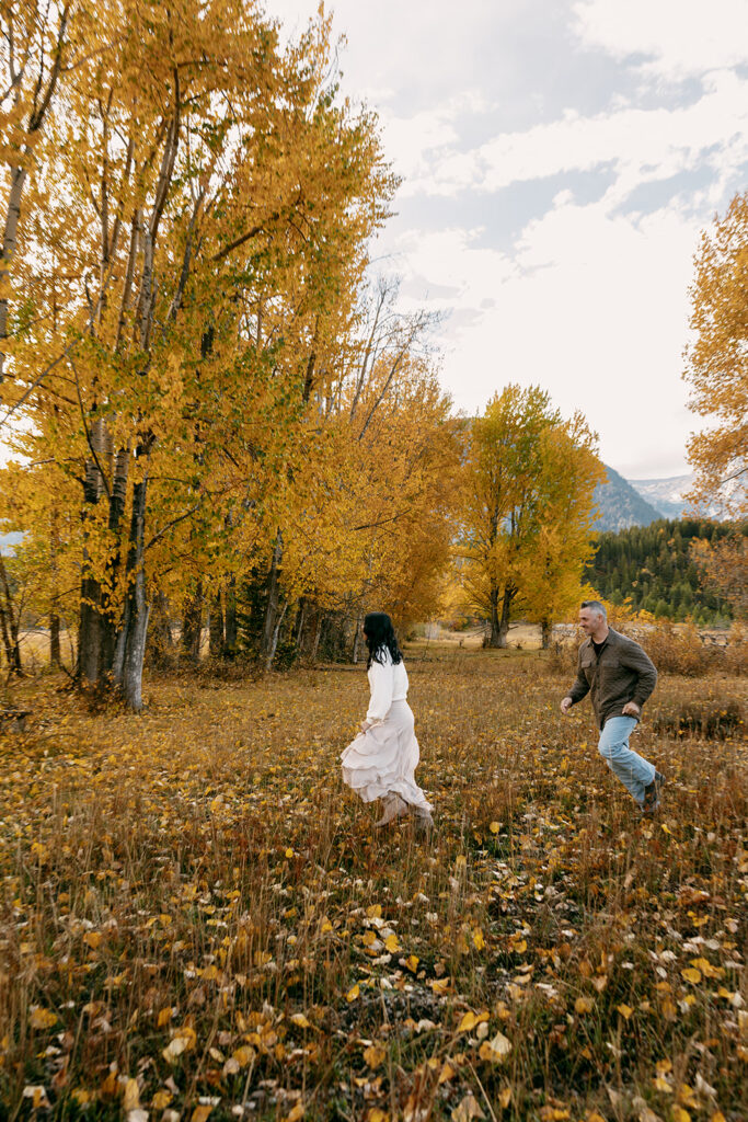 Couple runs through a field of golden aspen leaves near the base of the Tetons during fall engagement session.