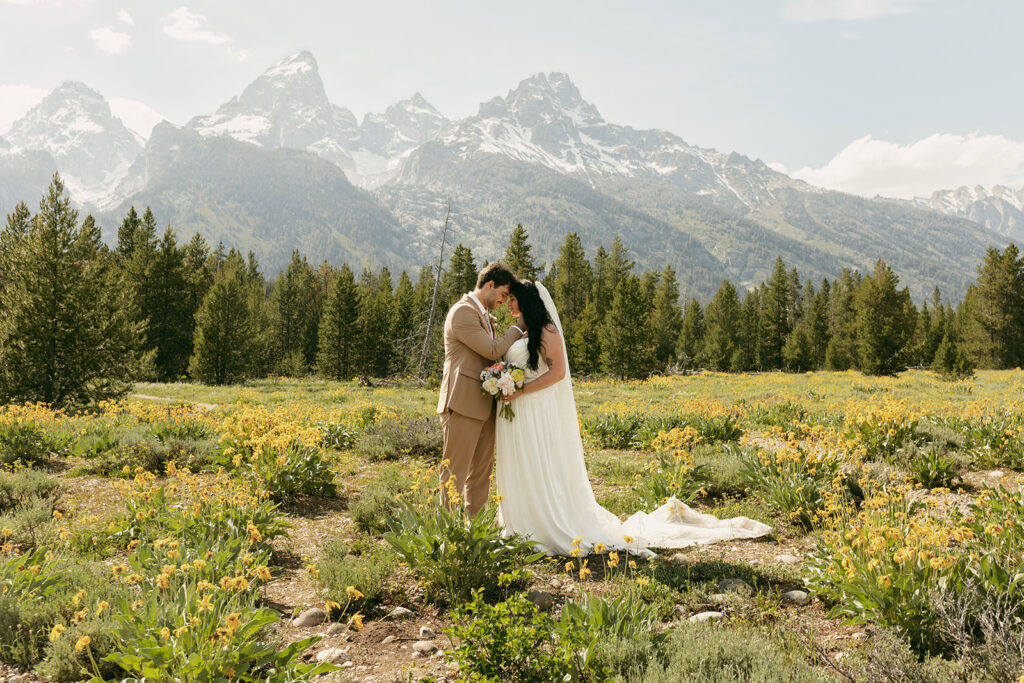 Bride and groom embrace in a wildflower field beneath the Teton peaks during their intimate wedding in the Grand Tetons.